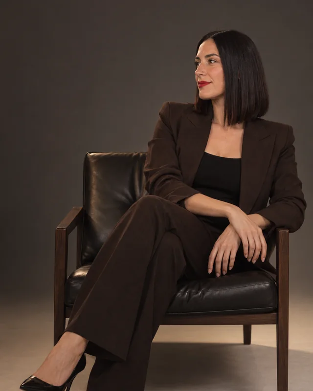 Retrato de Ángela Ruiz sentada en un sillón de cuero, con traje marrón, sobre un fondo de estudio oscuro.